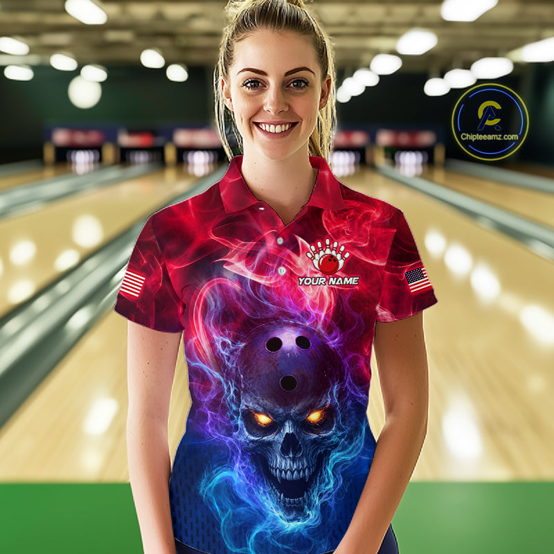 A woman stands in a bowling alley wearing a short-sleeve collared shirt with a vivid skull graphic in red, pink, purple, and blue. The shirt has a bowling pin motif on the chest, a small American flag on one sleeve, and 'YOUR NAME' printed on the front.