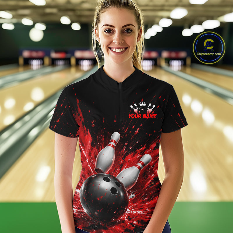 Woman wearing a black bowling quarter zip shirt with dramatic red splatter graphics, a large black bowling ball, and flying pins, plus custom player name text.