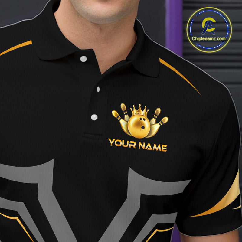 A close-up of a black polo shirt worn by a model, featuring a gold bowling pin and ball graphic with a crown and the text 'YOUR NAME' on the chest. The shirt has gold and gray graphic accents on the shoulders and sleeves.