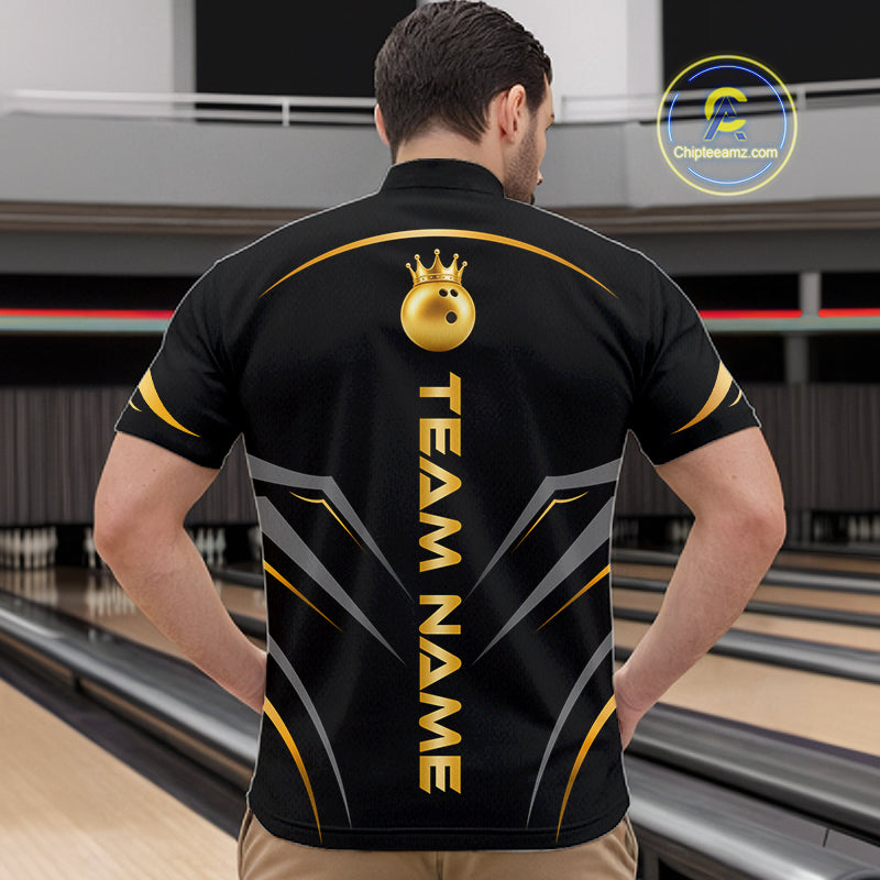 A man viewed from behind wearing a black short-sleeve bowling shirt with gold and gray graphic details, including a gold bowling ball with a crown and the text 'TEAM NAME' down the back. The background shows bowling lanes in a bowling alley.
