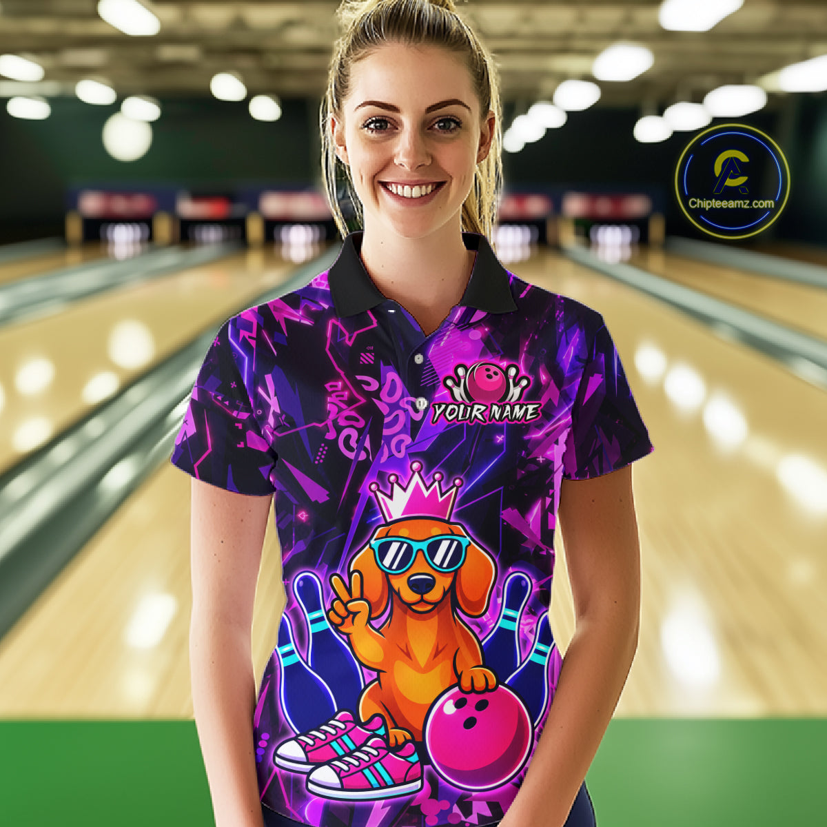 Woman wearing a black and purple bowling polo shirt featuring a cartoon dachshund wearing sunglasses and a crown, holding a pink bowling ball, with custom player name text.