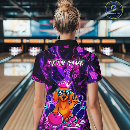 Woman wearing a black and purple bowling quarter zip shirt featuring a cartoon dachshund wearing sunglasses and a crown, holding a pink bowling ball, with custom team name text.