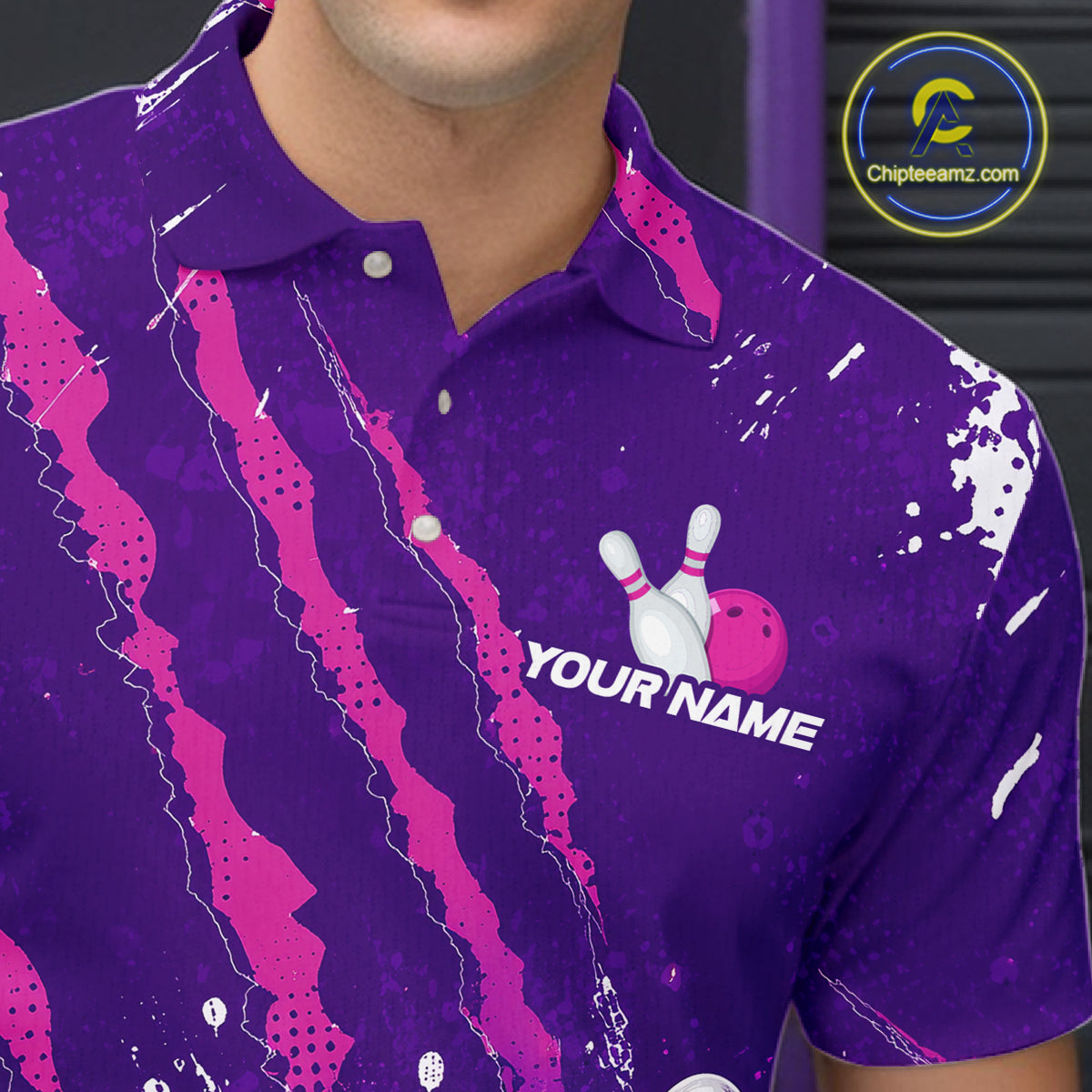 A close-up of a person wearing a purple short-sleeve polo shirt with bright pink abstract streaks, white paint splatter details, and a bowling-themed chest graphic with the text 'YOUR NAME'. A circular 'Chipeamz.