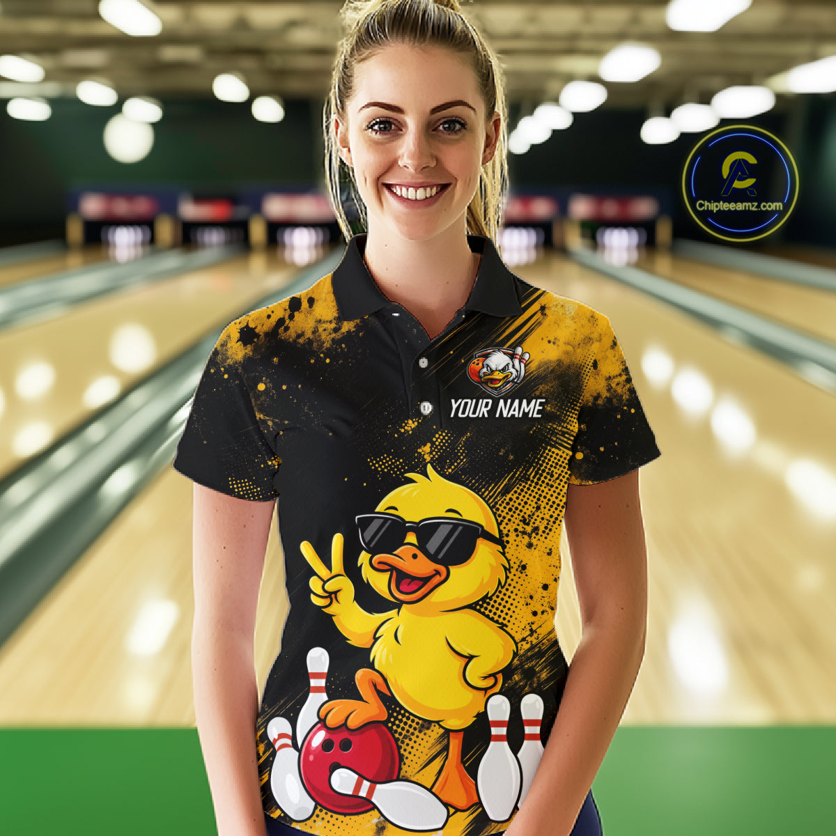 A woman standing in a bowling alley wearing a custom black and yellow polo shirt with a cartoon duck graphic, a bowling pin design, and the text 'YOUR NAME'.