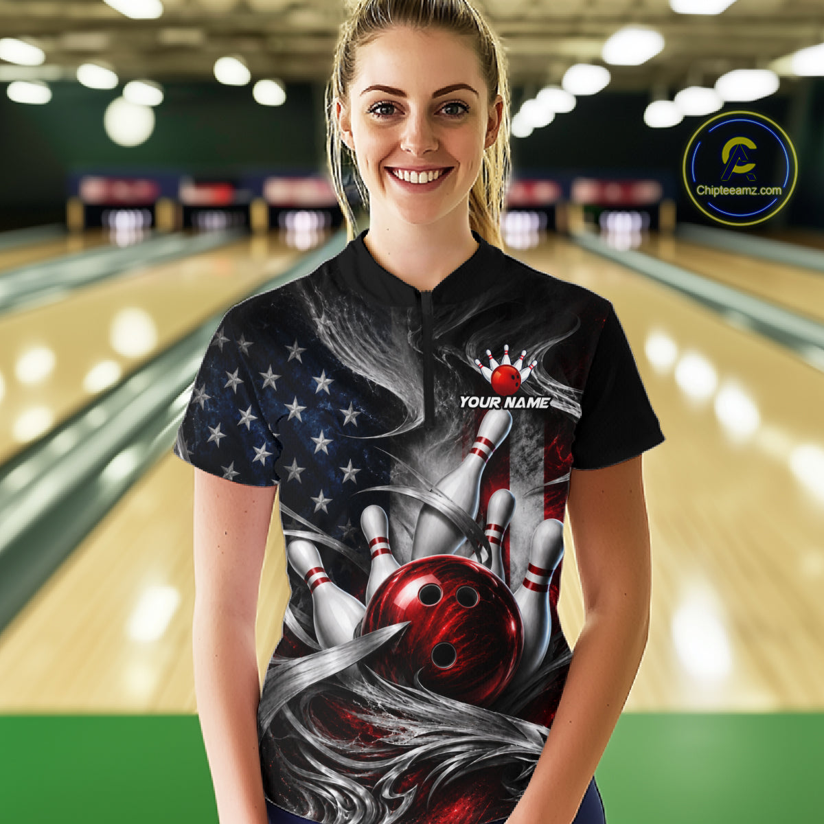 A woman stands in a bowling alley wearing a black short-sleeve bowling t-shirt with a custom graphic print featuring a red bowling ball, pins, and an American flag pattern. The shirt has a mock collar and 'YOUR NAME' printed on the chest.