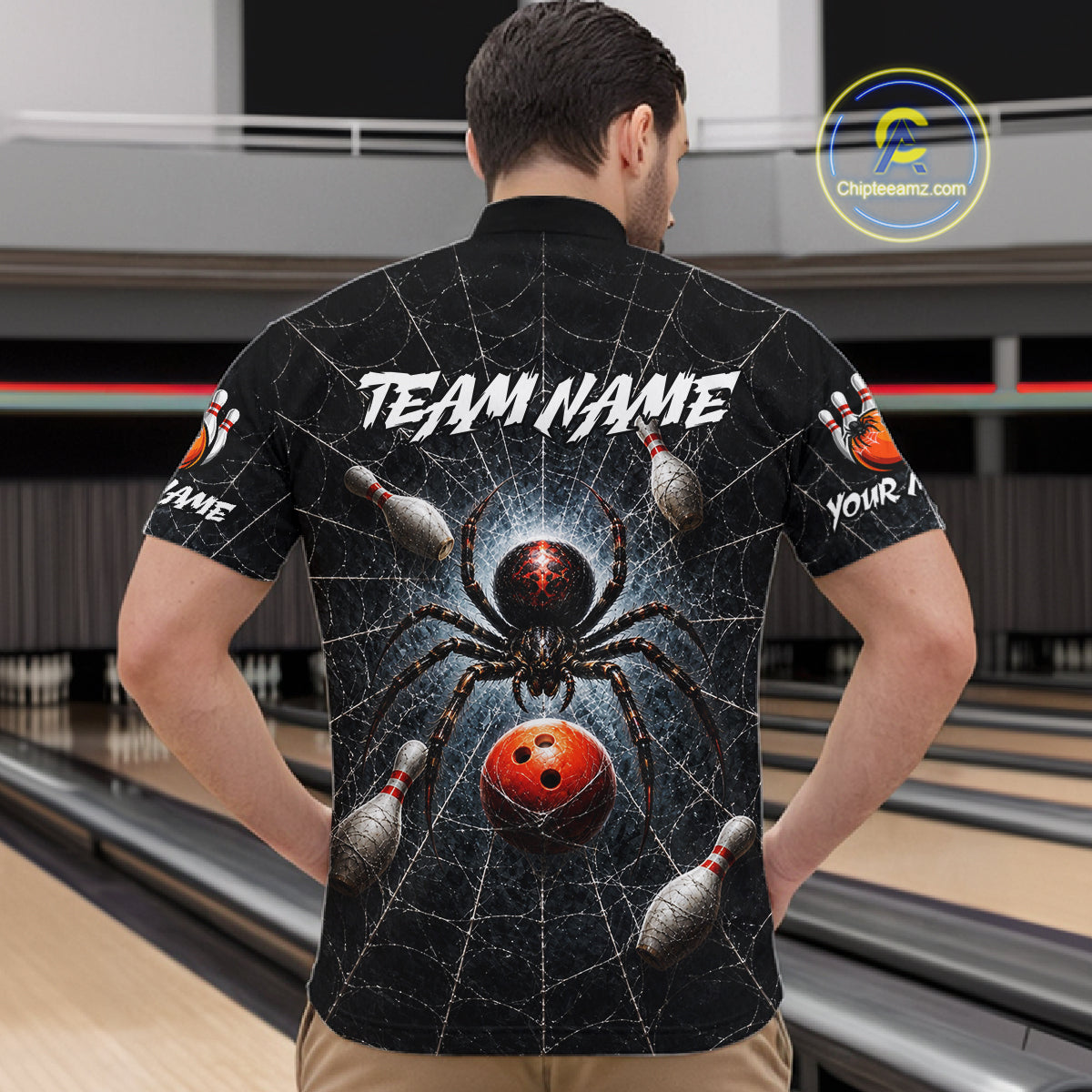A man viewed from behind wearing a black short-sleeve bowling-themed shirt with a large spider and bowling ball graphic on the back, standing in a bowling alley.