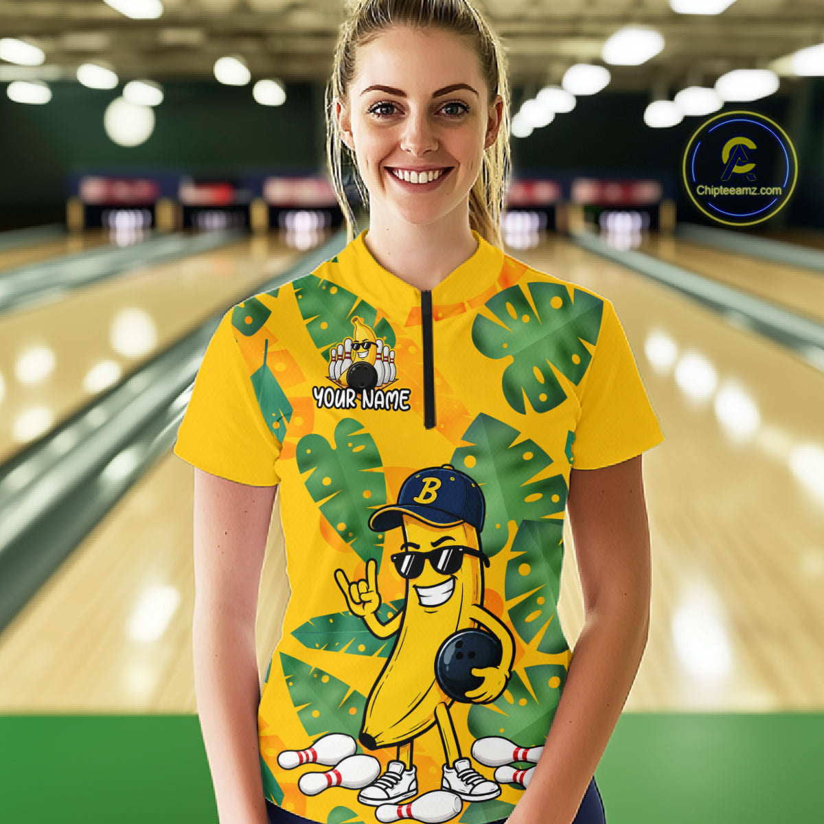 Woman in a bowling alley wearing a bright yellow tropical quarter zip shirt with green leaf patterns, custom team name text, and a smiling banana mascot holding a bowling ball.