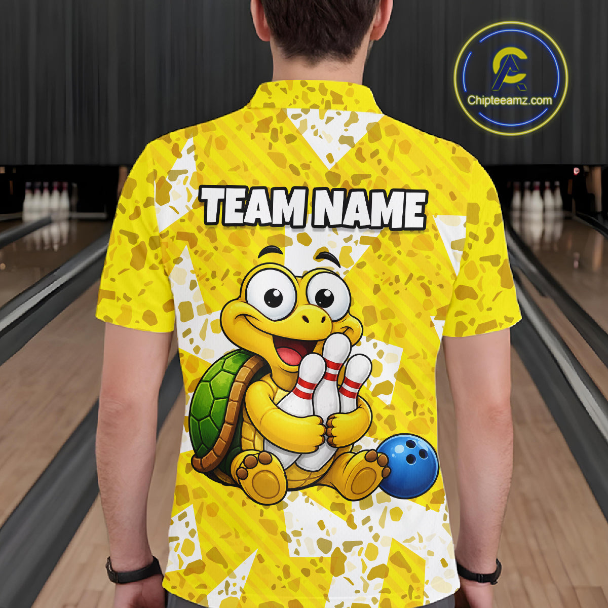 Man wearing a yellow bowling-themed shirt with a cartoon turtle holding a bowling ball and pins in a bowling alley.