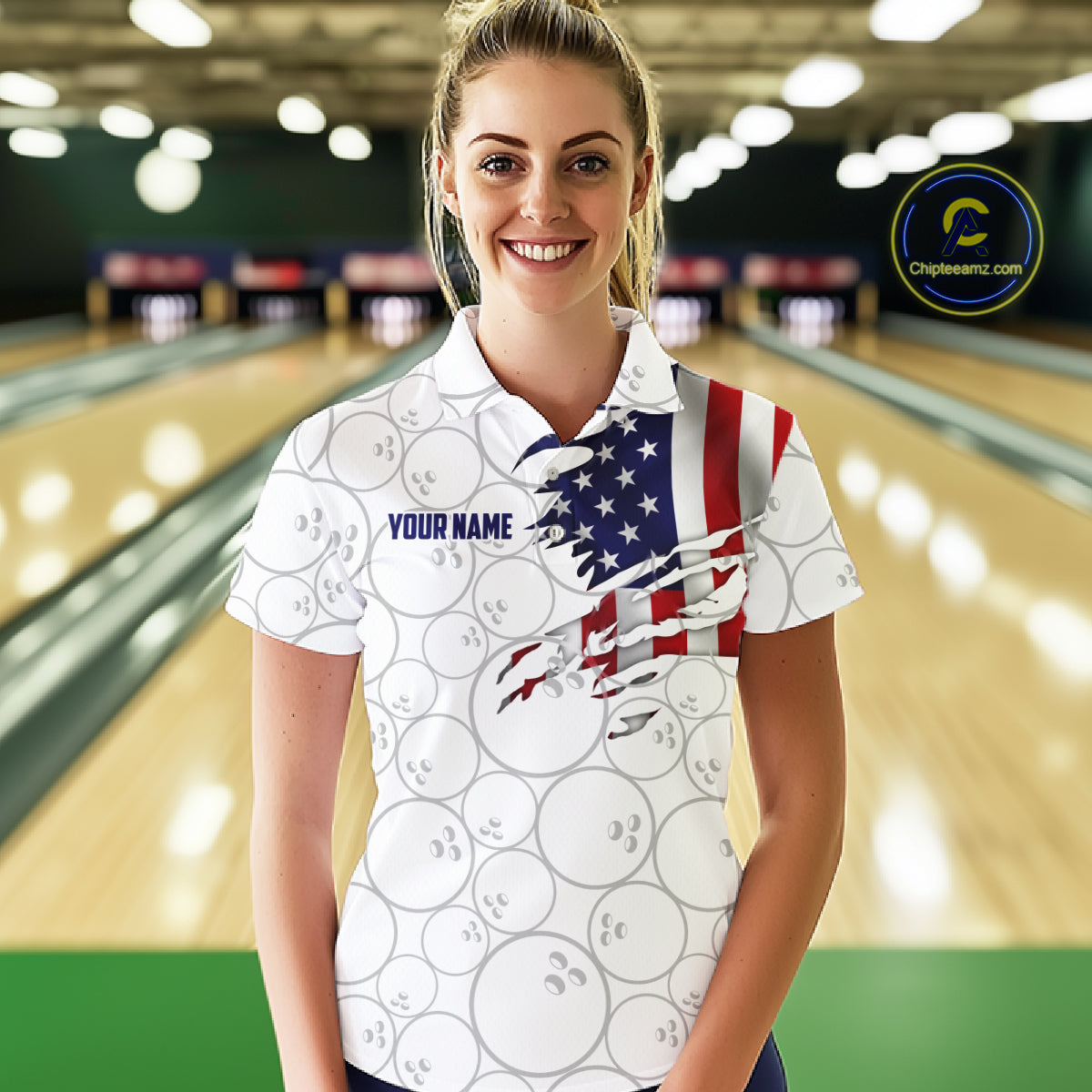 A woman stands in a bowling alley wearing a white short-sleeve polo shirt with bowling ball graphics and a distressed American flag design across the chest. The shirt includes the text 'YOUR NAME' for personalization.