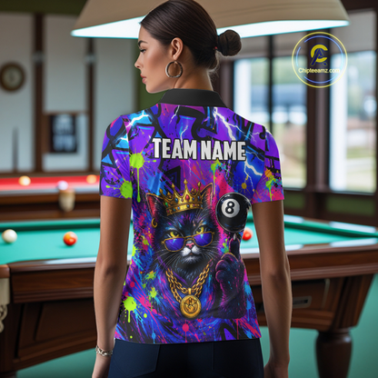 A woman stands in a billiards room wearing a short-sleeve collared shirt with a vivid all-over graphic print. The back of the shirt features a large black cat wearing a gold crown and sunglasses, a 8-ball, and the words 'TEAM NAME' in white.