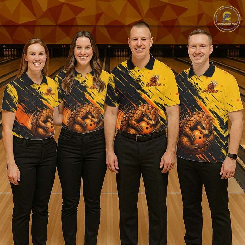 Four people standing in a bowling alley wearing matching yellow and black bowling shirts with a large bowling ball graphic on the front, paired with black pants. A bowling pin lane and wooden lanes are visible in the background.