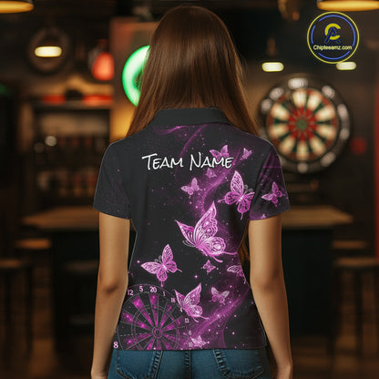 A woman viewed from behind wearing a dark short-sleeve polo shirt with a purple and pink butterfly and dartboard print, standing in a dimly lit bar environment.
