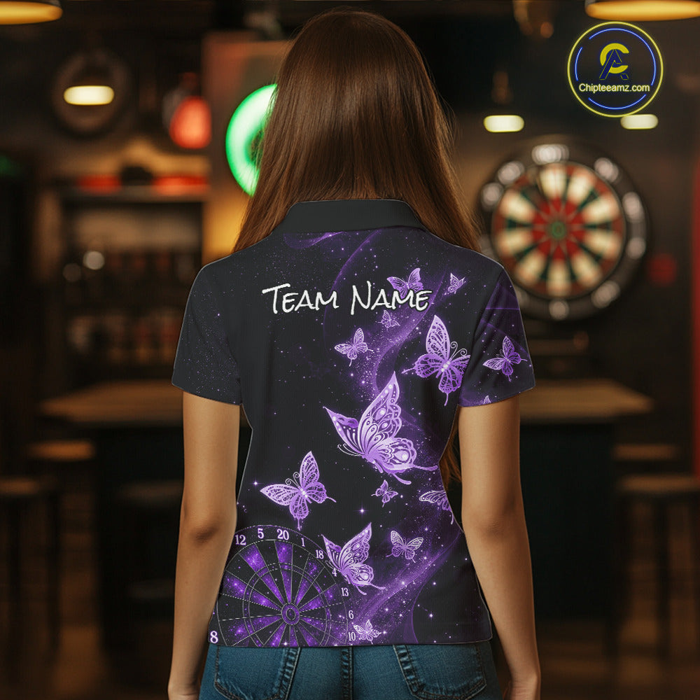A woman viewed from behind wearing a short-sleeve polo shirt with a purple and black butterfly and dartboard graphic design on the back, featuring the text 'TEAM NAME' across the upper back. The background is a dimly lit bar interior with a dartboard visible.