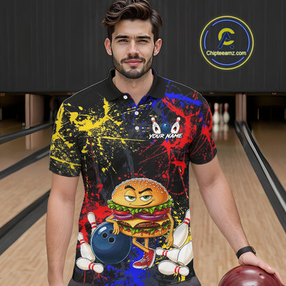 A man in a bowling alley wearing a black short-sleeve polo shirt with a colorful graphic print featuring a cartoon burger, bowling pins, bowling balls, and paint splatters. He is holding a bowling ball, with a circular 'ChipteeAmz'.