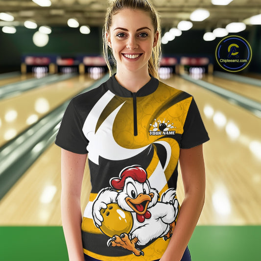 A woman stands in a bowling alley wearing a custom short-sleeve bowling shirt with a black, yellow, and white graphic design featuring a cartoon chicken holding a bowling ball. The background shows blurred bowling lanes.