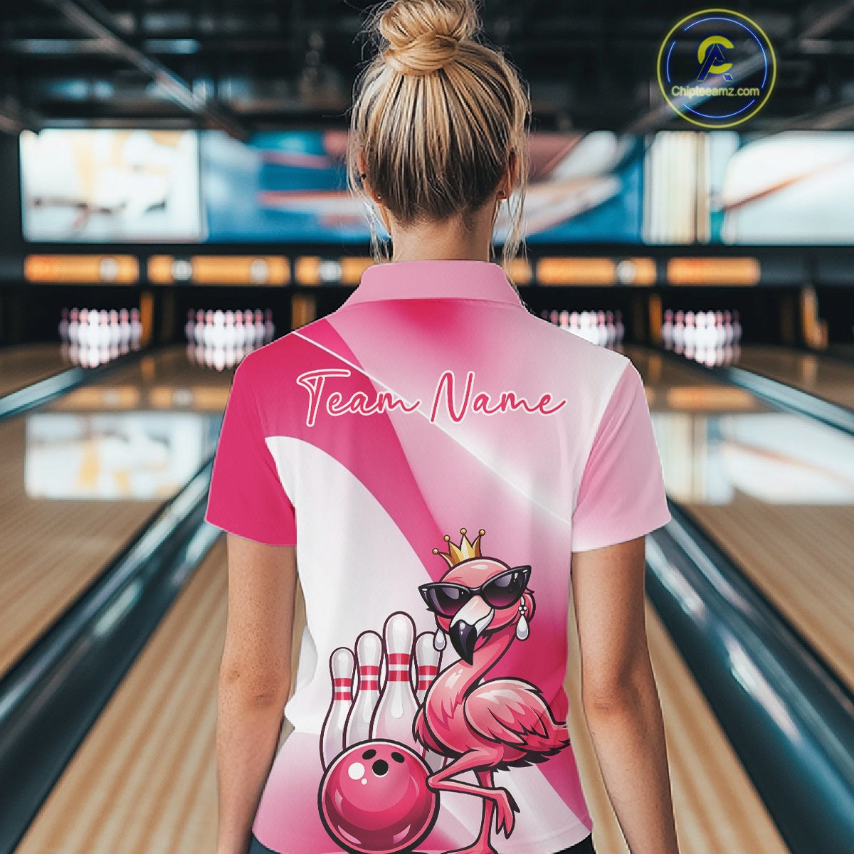 Back view of a female model in a bowling venue wearing a pink polo shirt featuring a crowned flamingo and bowling ball artwork.