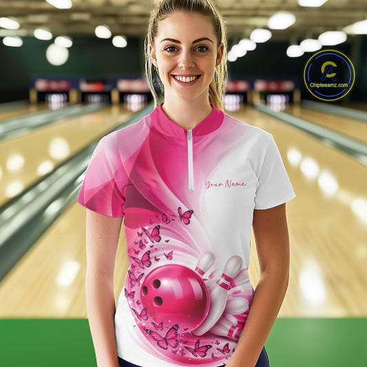 Front view of a female model in a white and pink bowling quarter zip featuring butterfly artwork and bowling graphics inside a bowling alley.