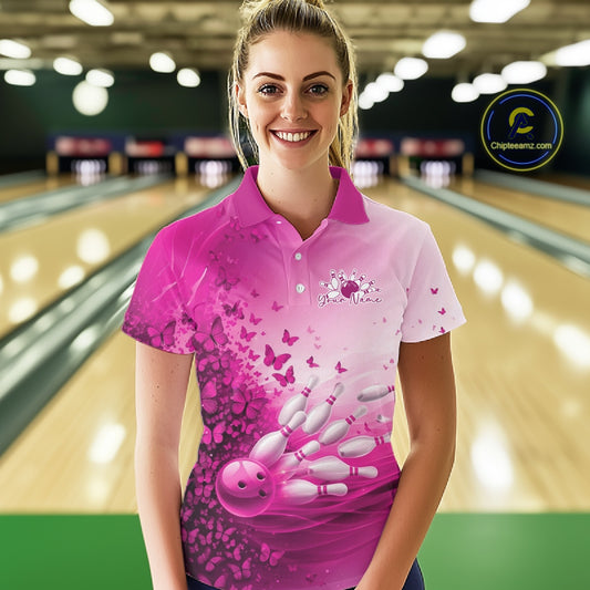 Female model wearing a white and pink bowling polo shirt with butterfly artwork and bowling-themed graphics at the bowling lane.