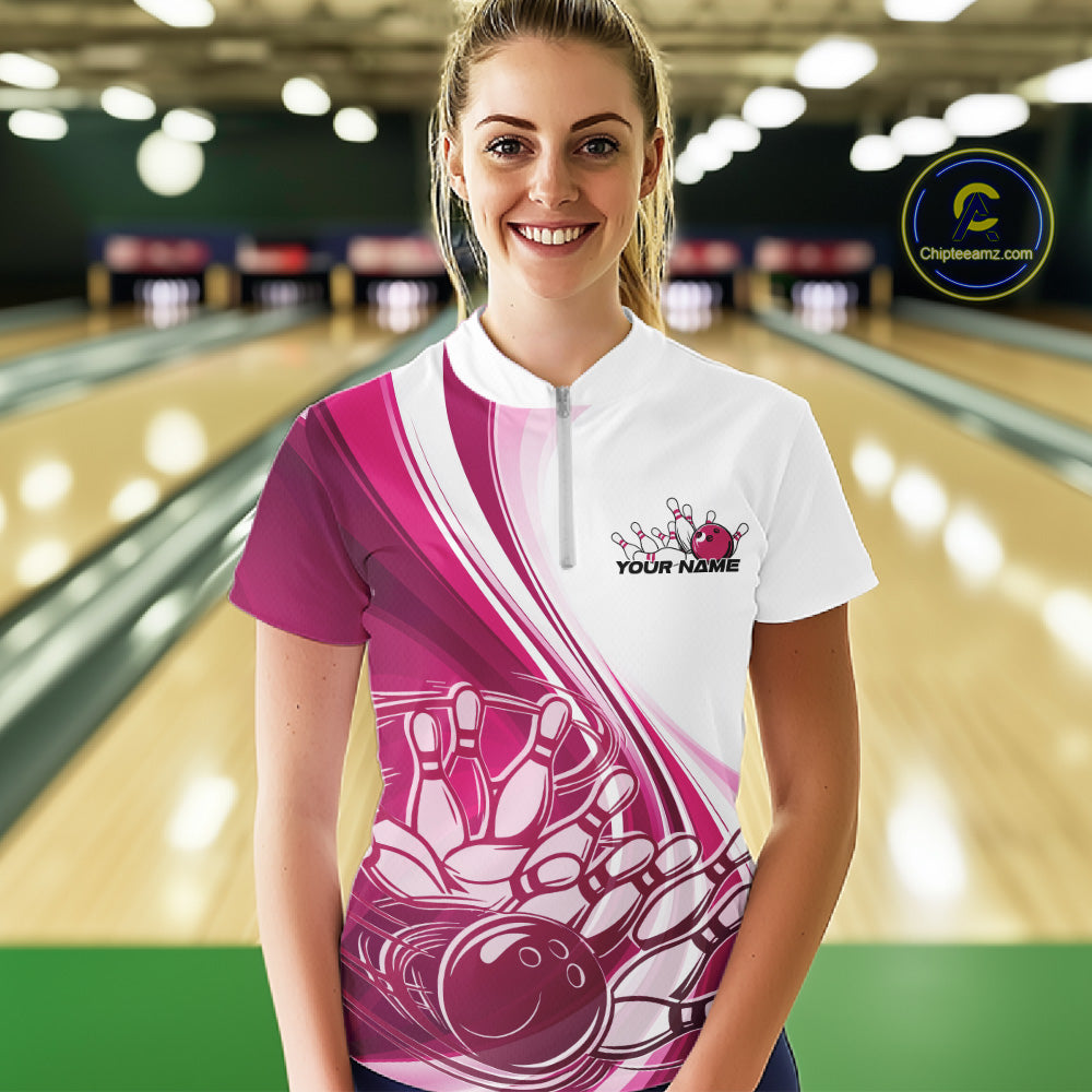 Female model wearing a white and pink bowling quarter zip with dynamic sweeping curves and a bowling ball crashing into pins artwork at the bowling lane.