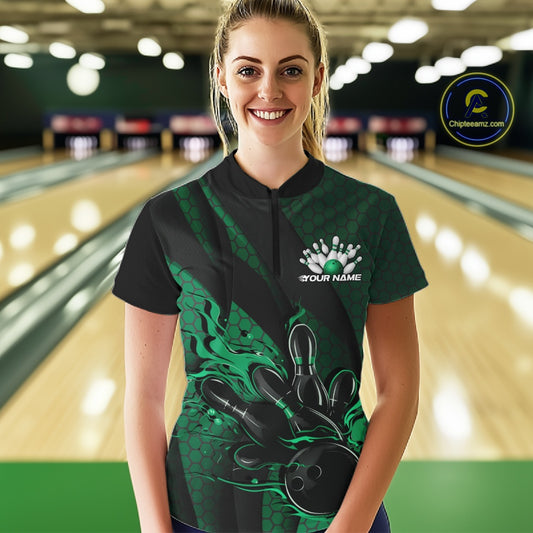 Female model in a bowling lane wearing black and green quarter zip shirt, front view featuring flaming bowling ball hitting pins with geometric stripe accents