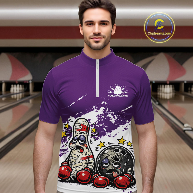 Male model at a bowling lane wearing a purple and white quarter-zip shirt, cartoon boxing-style bowling ball and pin artwork with playful tone.