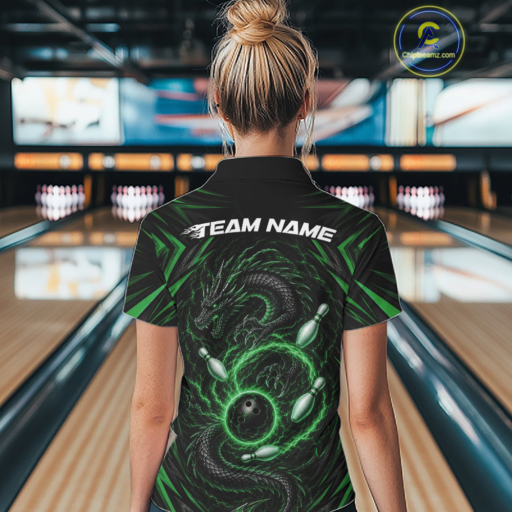 A woman viewed from behind wearing a black bowling quarter zip shirt with a green dragon graphic and 'TEAM NAME' printed across the back, standing in a bowling alley.