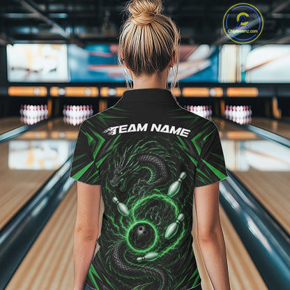 A woman viewed from behind wearing a black bowling quarter zip shirt with a green dragon graphic and 'TEAM NAME' printed across the back, standing in a bowling alley.