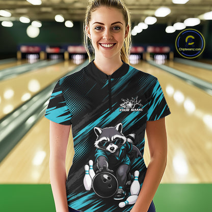 A woman stands in a bowling alley wearing a custom short-sleeve bowling quarter zip shirt. The shirt features a black and teal graphic design with a raccoon holding a bowling ball and pins