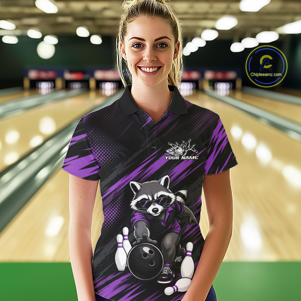 A woman stands in a bowling alley wearing a custom short-sleeve polo shirt with a raccoon bowling graphic and purple and black diagonal stripes. 