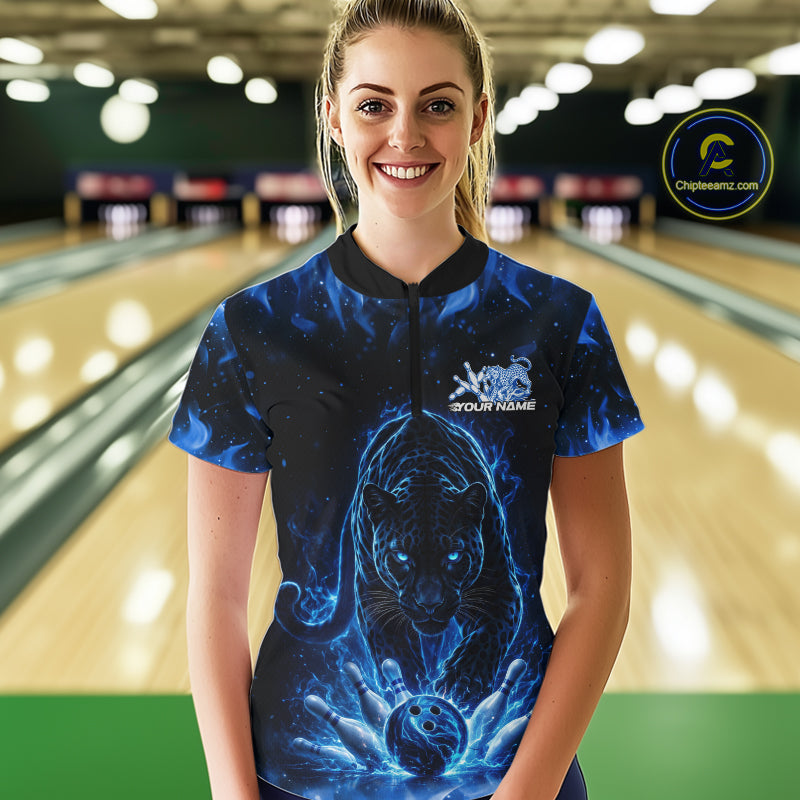 Front view of a female model in a bowling lane wearing a black quarter-zip shirt with glowing blue electric panther and dynamic bowling strike visuals.