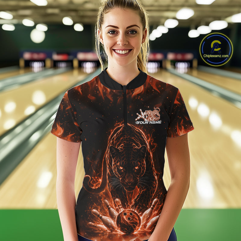 Front view of a female model in a bowling lane wearing a black quarter-zip shirt with glowing electric panther design and bowling ball striking pins in orange and black style.