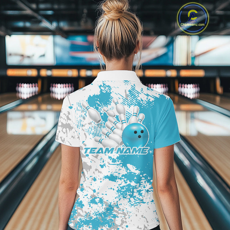 Back view female model in bowling alley wearing white polo with teal blue and white splatter design, relaxed stance near bowling lane