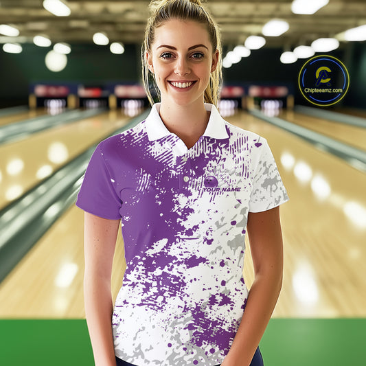 Female model front view at bowling lane wearing white polo shirt with purple and white splatter design, sporty bowling center scene