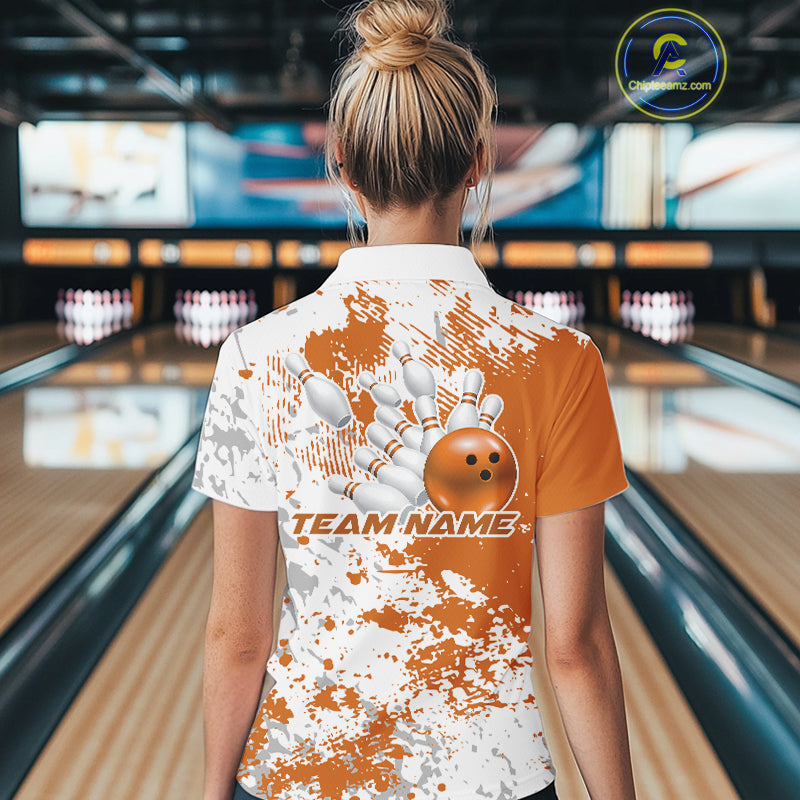 Back view female model in bowling venue wearing white polo with orange and white splatter pattern, standing near bowling lane