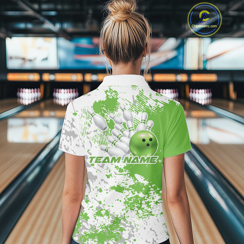 Back view female model at bowling lane wearing white polo with green and white splatter background, relaxed stance inside bowling center