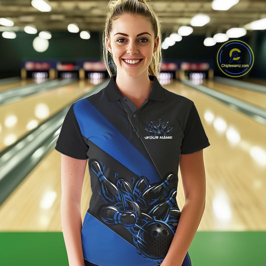 Female model front view in bowling venue wearing black and blue polo shirt with flaming bowling ball knocking down pins in energetic action scene.
