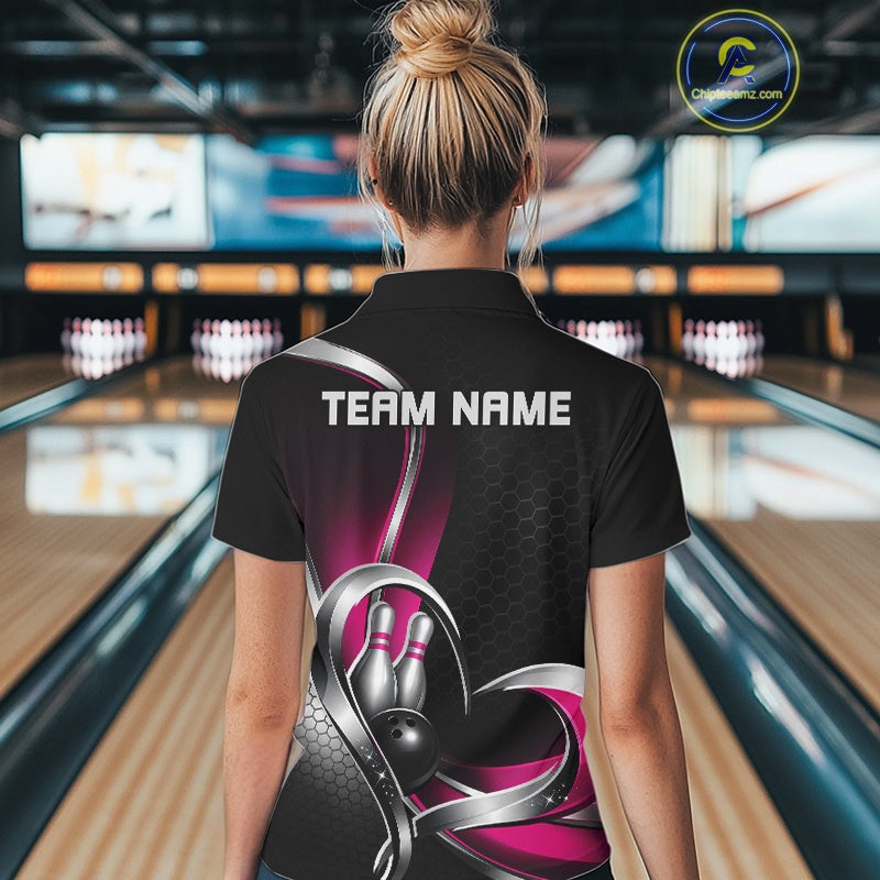 Back view of a female model in a bowling lane wearing a black and pink quarter zip shirt, displaying a honeycomb pattern with a heart-shaped motif around a bowling ball and pins.