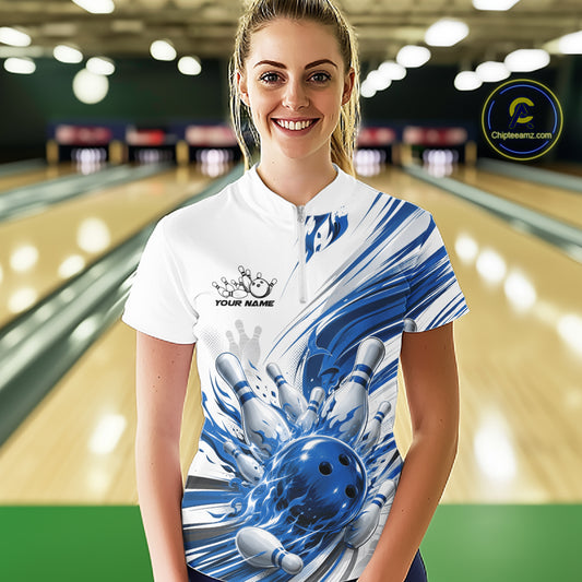 A woman stands in a bowling alley wearing a white short-sleeve polo shirt with a blue bowling-themed graphic print featuring a bowling ball and pins, with customizable text on the chest.