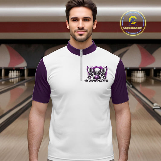 A man stands in a bowling alley wearing a bowling shirt with quarter zip collar, purple skull-themed bowling graphic with black wings, pins, bowling ball