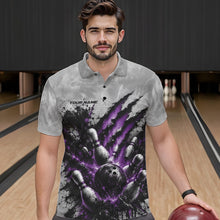 Load image into Gallery viewer, Male model shown from the front wearing a gray bowling polo shirt featuring a dramatic purple bowling ball striking pins graphic with claw-mark artwork at a bowling lane.