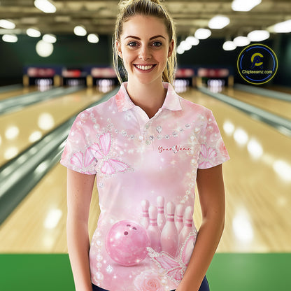 Female model in a bowling center wearing a bowling polo shirt with glitter butterfly accents, roses, bowling pins, and a bowling ball illustration.