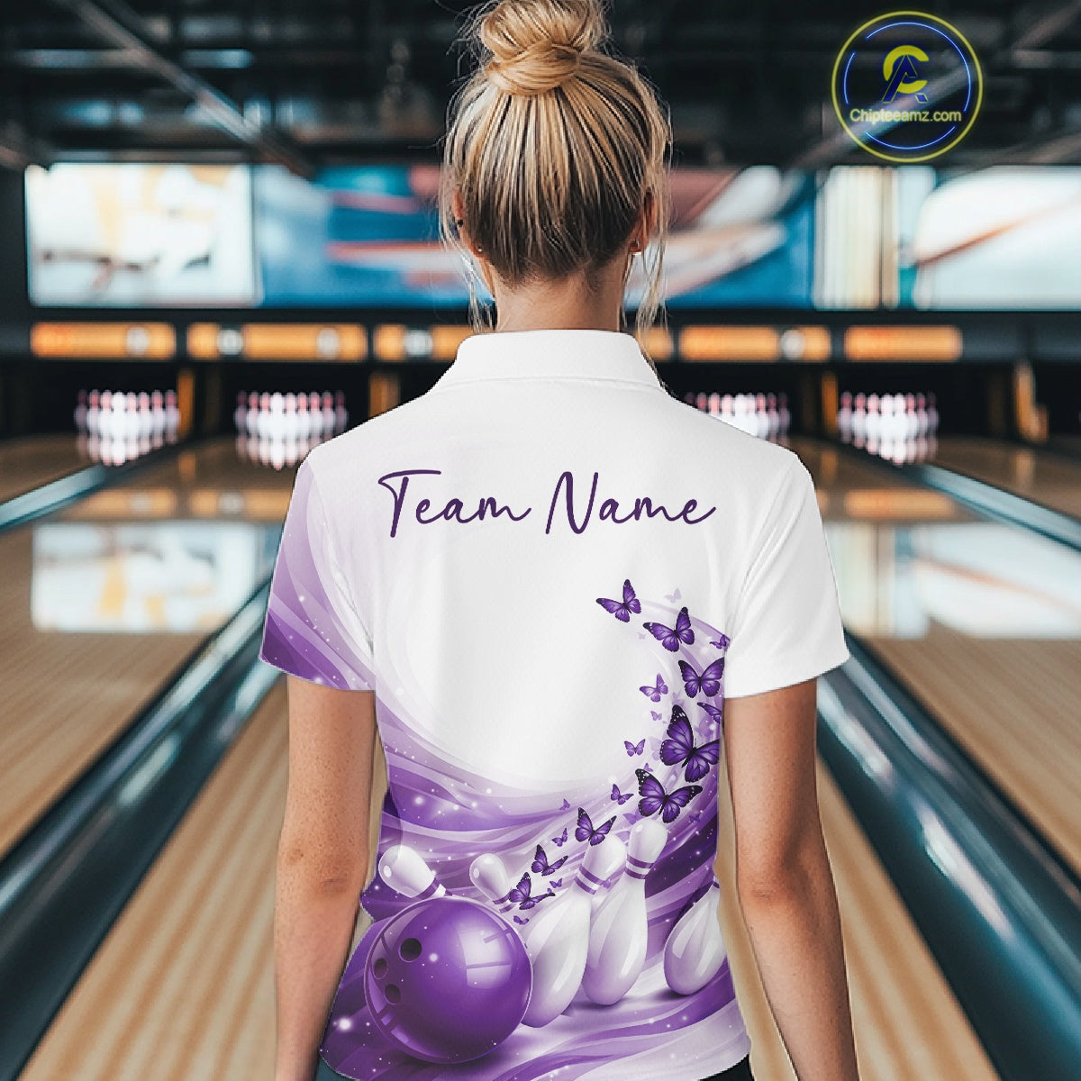 Back view of a white and purple bowling quarter zip with butterfly accents and bowling graphics inside a bowling center.