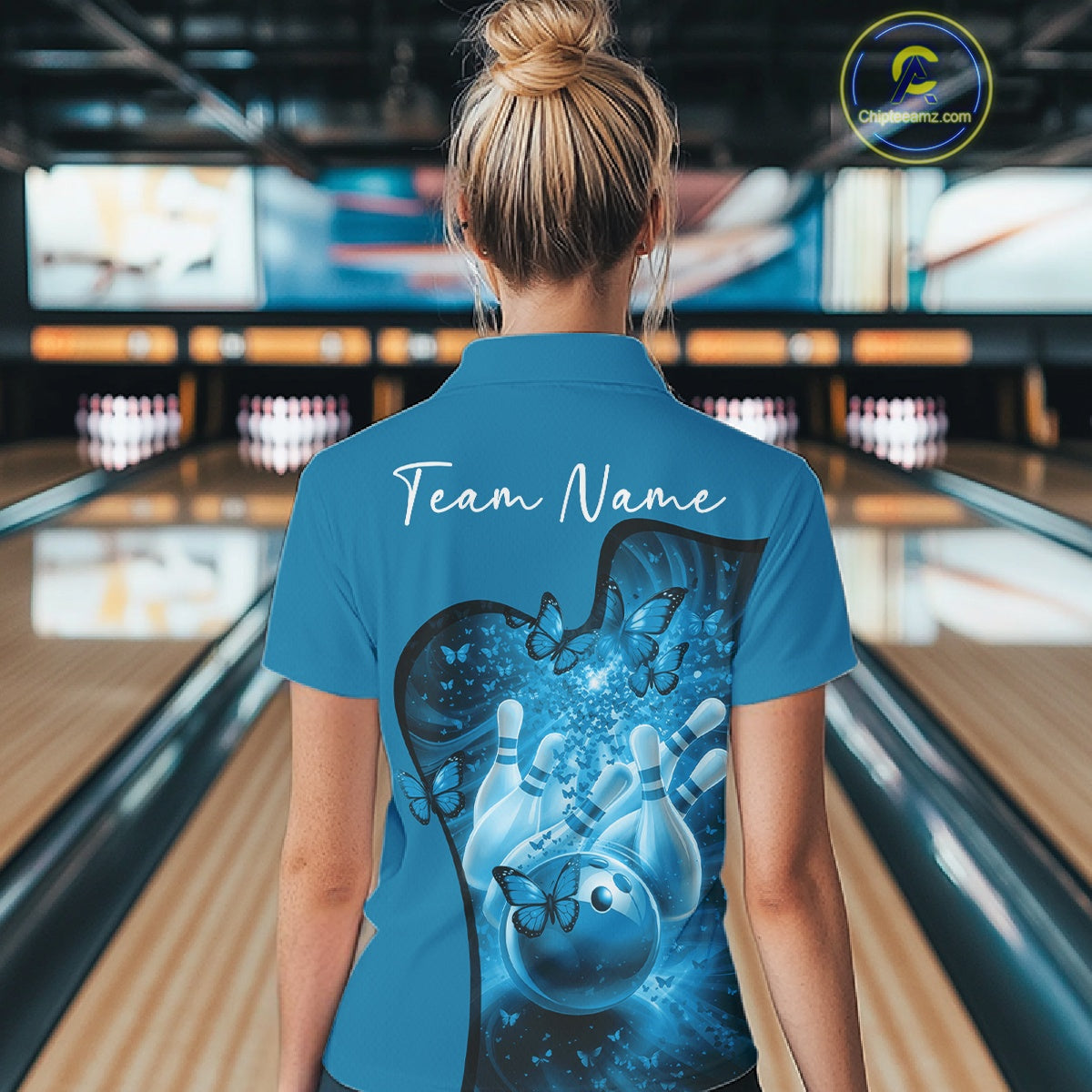 Back view of a female model wearing a blue bowling polo with butterfly artwork and bowling-themed graphics