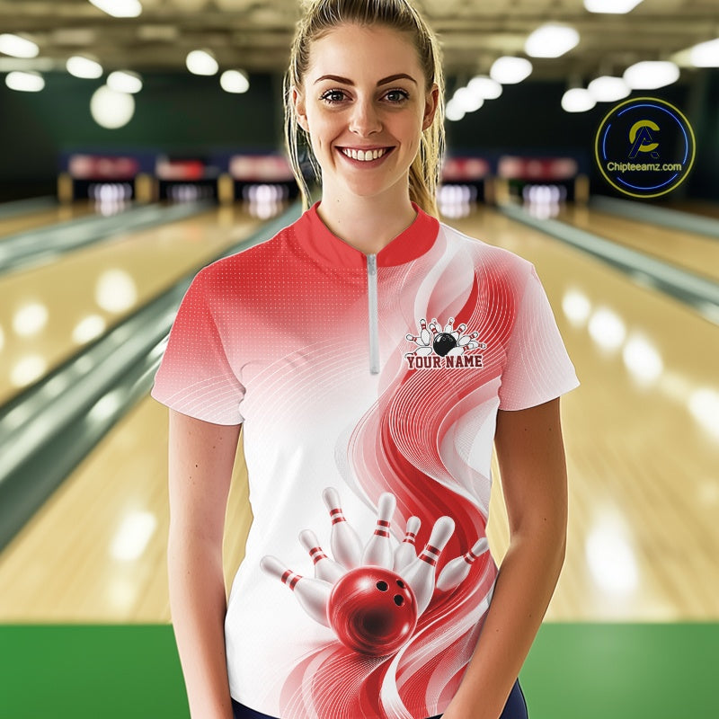 Female model in a white and red bowling quarter zip with flowing wave artwork and glossy bowling strike graphics, front view at the bowling lane