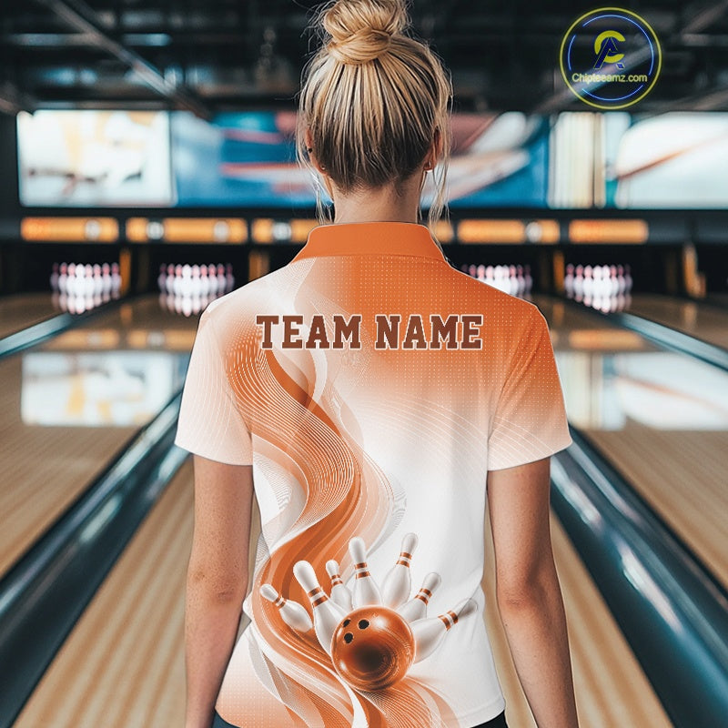 Female model standing in a bowling lane showing the back of a white and orange bowling quarter-zip shirt with abstract wave lines and a glossy bowling ball striking pins graphic.