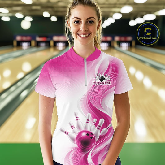 Female model wearing a white and pink bowling quarter zip with flowing abstract wave accents and a glossy bowling ball striking pins at the bowling lane