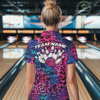 Back view of a woman standing at a bowling alley, wearing a gold, brown, and black leopard-print bowling polo with “Team Name” and bowling pins on the back.