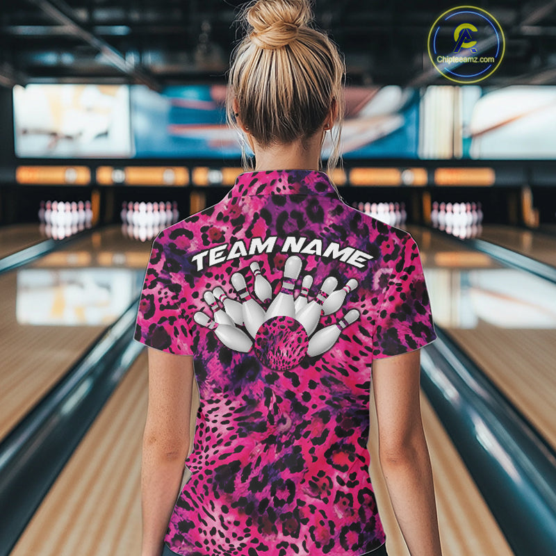 Back view of a woman standing at a bowling alley, wearing a pink, purple, and black leopard-print bowling polo with “Team Name” and bowling pins on the back.
