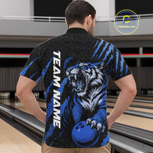 Load image into Gallery viewer, Front view of a male model at a bowling lane wearing a black and mid blue bowling quarter-zip shirt featuring a roaring tiger holding a mid blue bowling ball with coordinated claw-stripe graphics and a geometric background pattern.