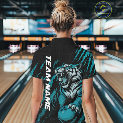 Back view of a female model wearing a black and teal blue bowling quarter-zip shirt at a bowling lane, featuring a roaring tiger holding a teal blue bowling ball with teal blue claw-stripe artwork and a geometric background pattern.